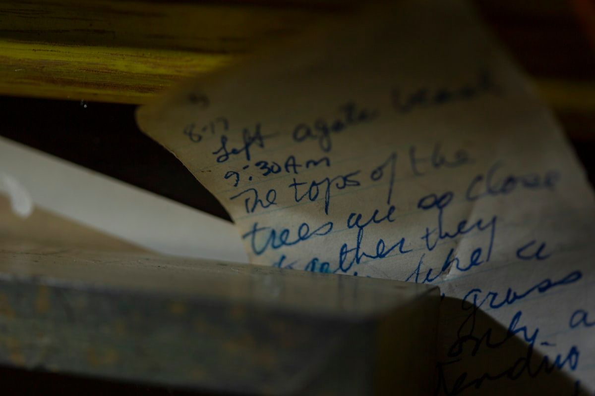 A kitchen table covered with organized storm-damage evidence: printed roof photos, a notepad with handwritten storm details, a stack of repair receipts, an inspection report, a rolled-up tarp sample, and a few broken shingle and tile fragments beside them